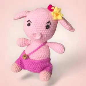 Charmant cochon rose en crochet avec une salopette violette et une coiffe fleurie.