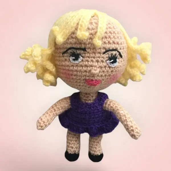 Petite poupée au crochet avec une jupe violette et des cheveux bouclés.