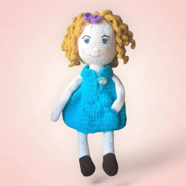 Poupée en crochet aux cheveux blonds frisés et portant une robe bleue.