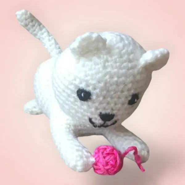 Adorable chat blanc en crochet avec une balle rose.